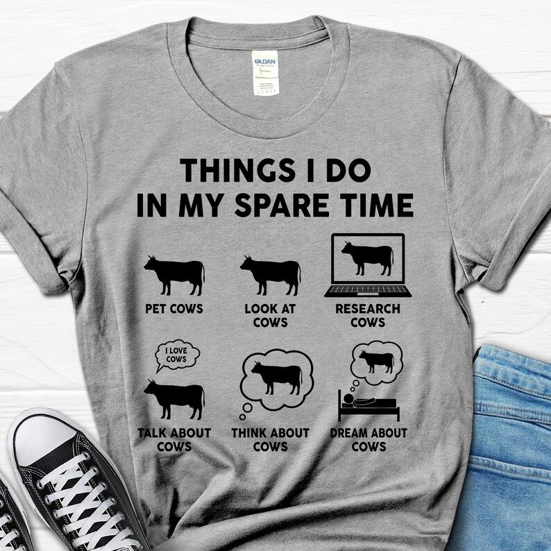 以下が含まれることがあります： 「Things I do in my spare time」というテキストと、牛に関連する活動のリストが書かれたグレーのTシャツ。リストには、「牛をなでる」、「牛を見る」、「牛を調べる」、「牛について話す」、「牛について考える」、「牛の夢を見る」などが含まれています。