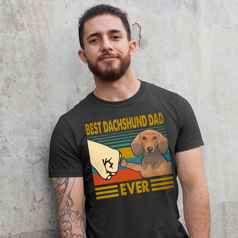 May include: A dark grey t-shirt with a vintage-style graphic of a dachshund giving a high five. The graphic says "Best Dachshund Dad Ever".