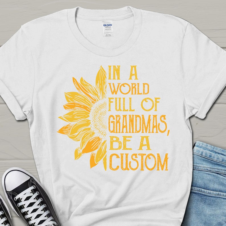 May include: White t-shirt featuring a yellow sunflower graphic and the text "In a world full of grandmas, be a custom".
