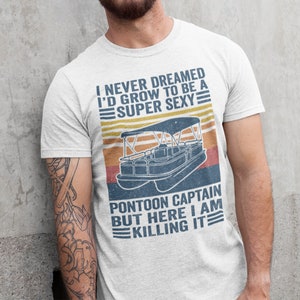 Pu&ograve; includere: Una maglietta bianca con una grafica in stile vintage di una barca pontone. Il testo sulla maglietta recita "I never dreamed I'd grow to be a super sexy pontoon captain but here I am killing it."