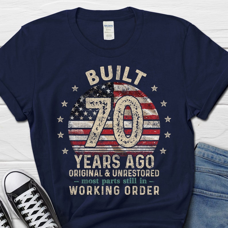 May include: Navy blue t-shirt with a distressed American flag design and the text "Built 70 Years Ago - Original & Unrestored - Most parts still in working order".