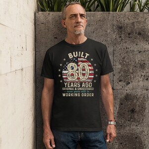 May include: Black t-shirt with a vintage American flag design and the text "BUILT 80 YEARS AGO ORIGINAL & UNRESTORED - most parts still in - WORKING ORDER".