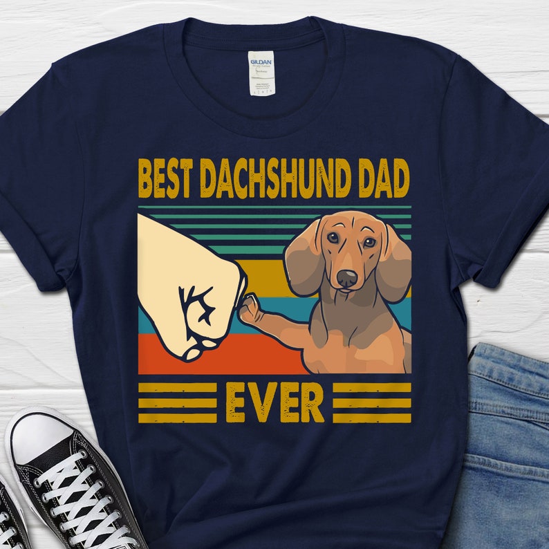 May include: Navy blue t-shirt with a retro-style graphic of a dachshund dog and the text "Best Dachshund Dad Ever".