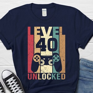 May include: A navy blue t-shirt with a vintage-style graphic that says "Level 40 Unlocked" with a retro video game controller.