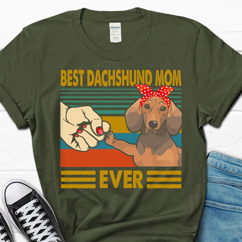 May include: Green t-shirt with a retro-style graphic of a dachshund wearing a red bandana. The text "Best Dachshund Mom Ever" is printed on the shirt.