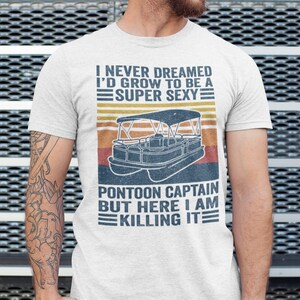 Pu&ograve; includere: Una maglietta bianca con una grafica in stile vintage di una barca pontone e il testo "Non avrei mai pensato di diventare un capitano di pontone super sexy, ma ecco, lo sto uccidendo."