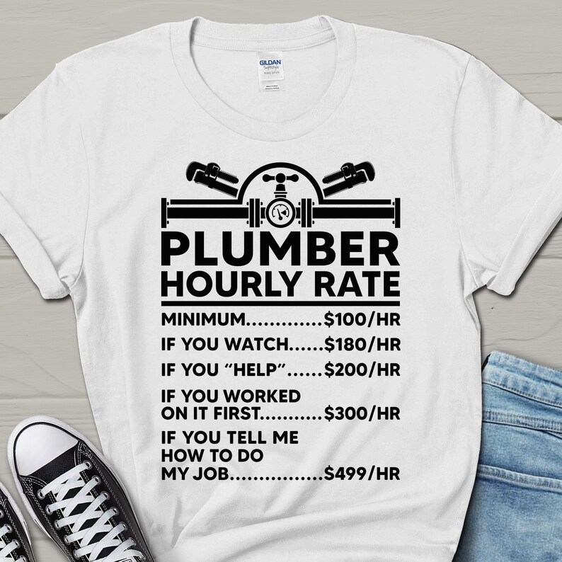 May include: White t-shirt with a black graphic of a plumber's tools and the text "Plumber Hourly Rate". The graphic includes a wrench, pipe, and valve. The text below the graphic lists different hourly rates for a plumber based on the level of assistance provided.  The rates are: $100/hr, $180/hr, $200/hr, $300/hr, and $499/hr.