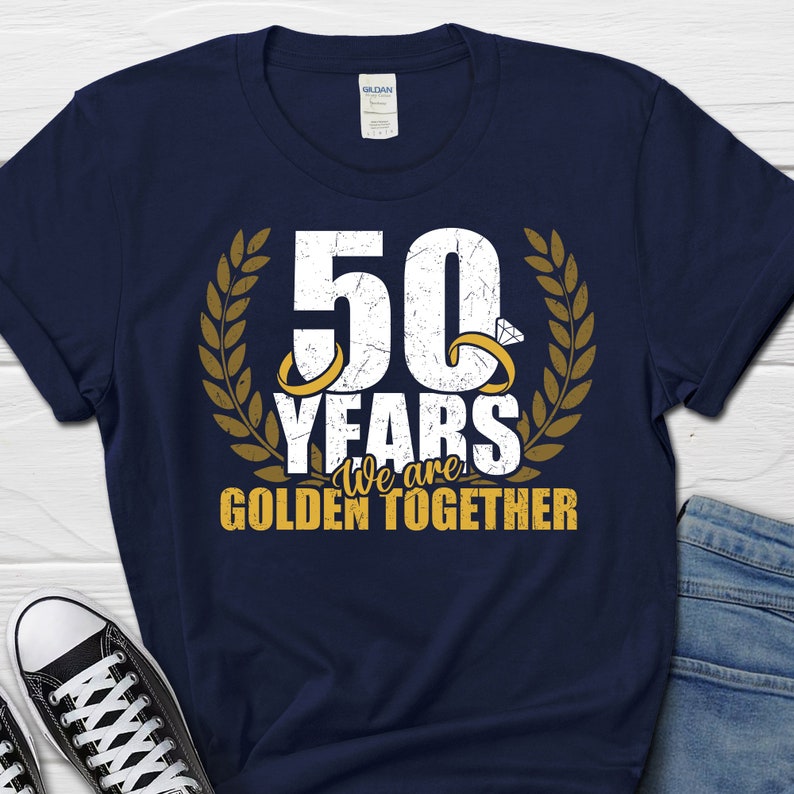 May include: Navy blue t-shirt with a white distressed graphic that says "50 Years We are Golden Together". The graphic includes two gold rings with diamonds and a laurel wreath.