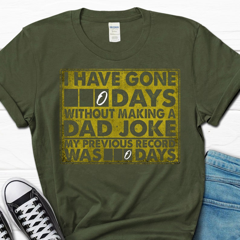 Op de afbeelding: Een groen T-shirt met een gele afbeelding waarop staat: "Ik ben 0 dagen zonder een vaders grapje gegaan. Mijn vorige record was 0 dagen."