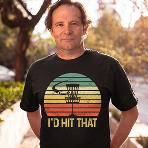 May include: A black t-shirt with a vintage-style graphic of a disc golf basket and the text "I'd Hit That".
