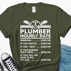 May include: Green t-shirt with white text that reads "Plumber Hourly Rate" and a list of hourly rates for different levels of assistance. The rates are: Minimum - $100/hr, If you watch - $180/hr, If you "help" - $200/hr, If you worked on it first - $300/hr, If you tell me how to do my job - $499/hr.