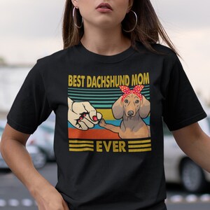 May include: Black t-shirt with a vintage-style graphic of a dachshund wearing a red bandana. The graphic says "Best Dachshund Mom Ever".