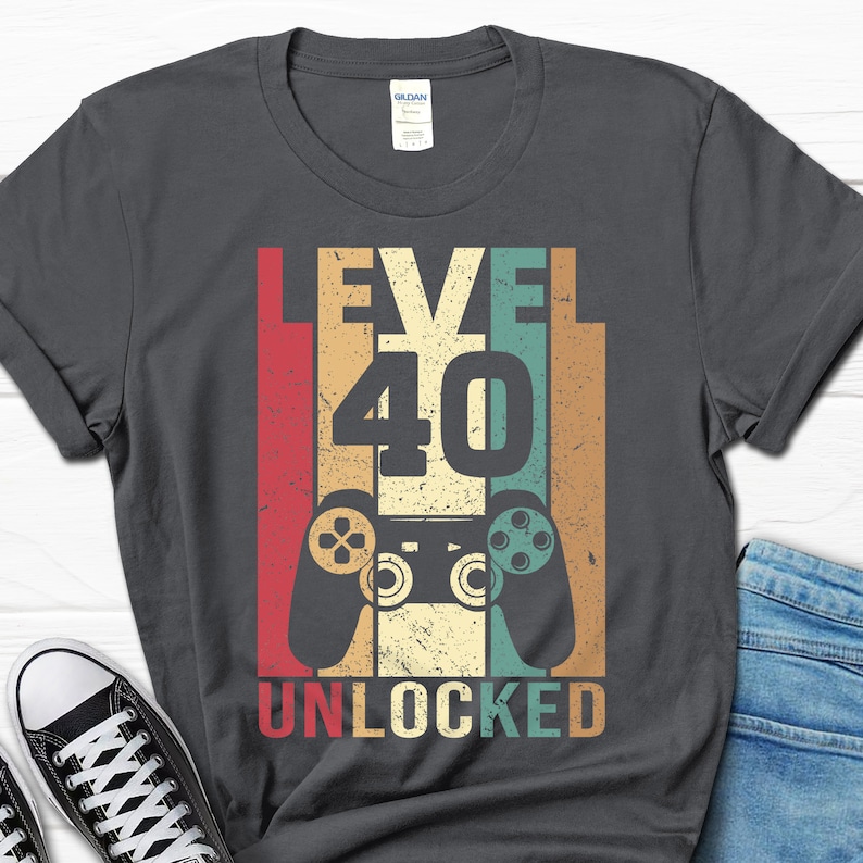 May include: A dark gray t-shirt with a vintage-style graphic that says "Level 40 Unlocked" with a retro video game controller in the center.