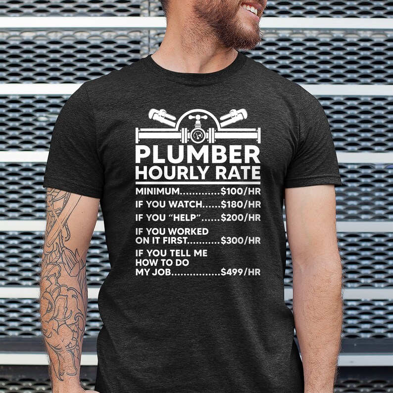 May include: A black t-shirt with a white graphic of a plumber's tools and the text "Plumber Hourly Rate". The graphic includes a pipe, a wrench, and a valve. The text below the graphic lists different hourly rates for different levels of assistance, from a minimum of $100/hr to $499/hr for telling the plumber how to do their job.