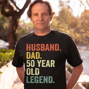 May include: A black t-shirt with a vintage-style graphic that reads "Husband. Dad. 50 Year Old Legend."