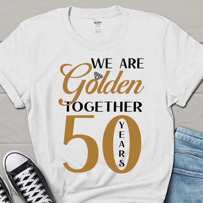 May include: White t-shirt with black text that reads "We are Golden Together 50 Years" with a diamond graphic above the word "Golden". The number 50 is in gold with the word "Years" vertically written in black inside the number.