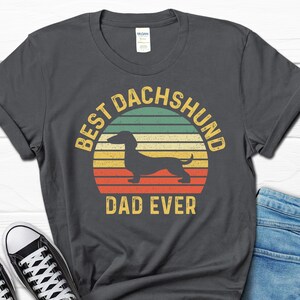 May include: A dark gray t-shirt with a vintage-style graphic of a dachshund and the text "Best Dachshund Dad Ever".