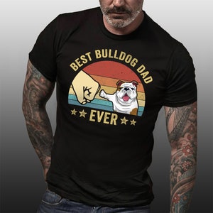 May include: Black t-shirt with a vintage-style graphic of a bulldog giving a fist bump. The graphic says "Best Bulldog Dad Ever" with stars on either side of the word "Ever".