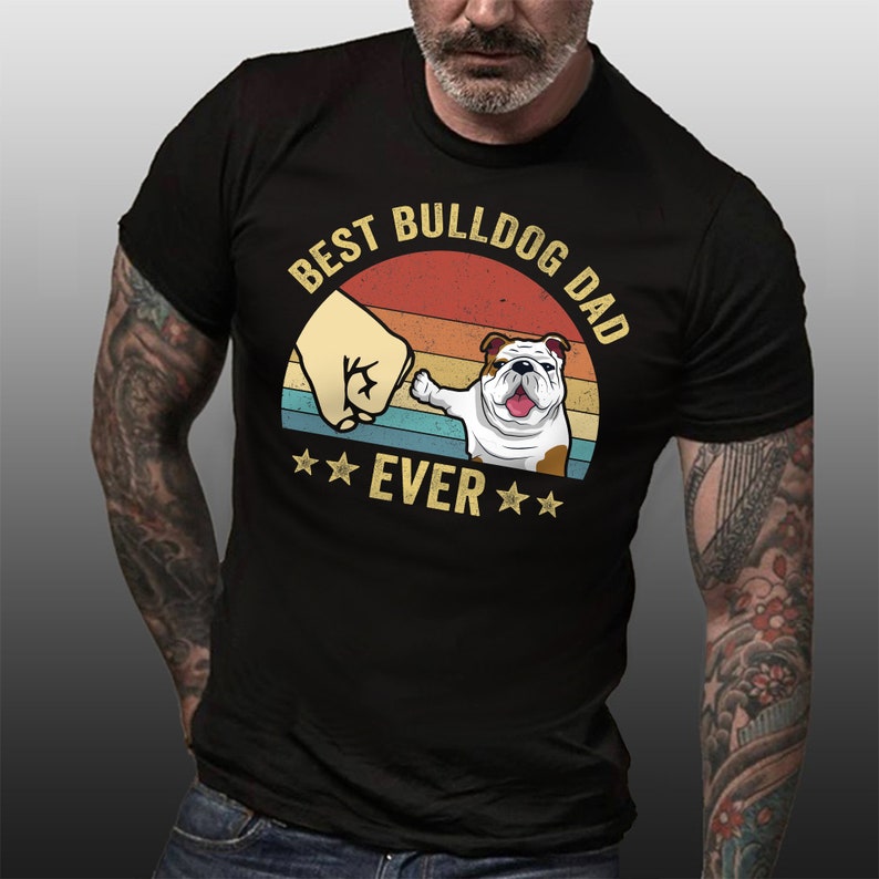 May include: Black t-shirt with a vintage-style graphic of a bulldog giving a fist bump. The graphic says "Best Bulldog Dad Ever" with stars on either side of the word "Ever".