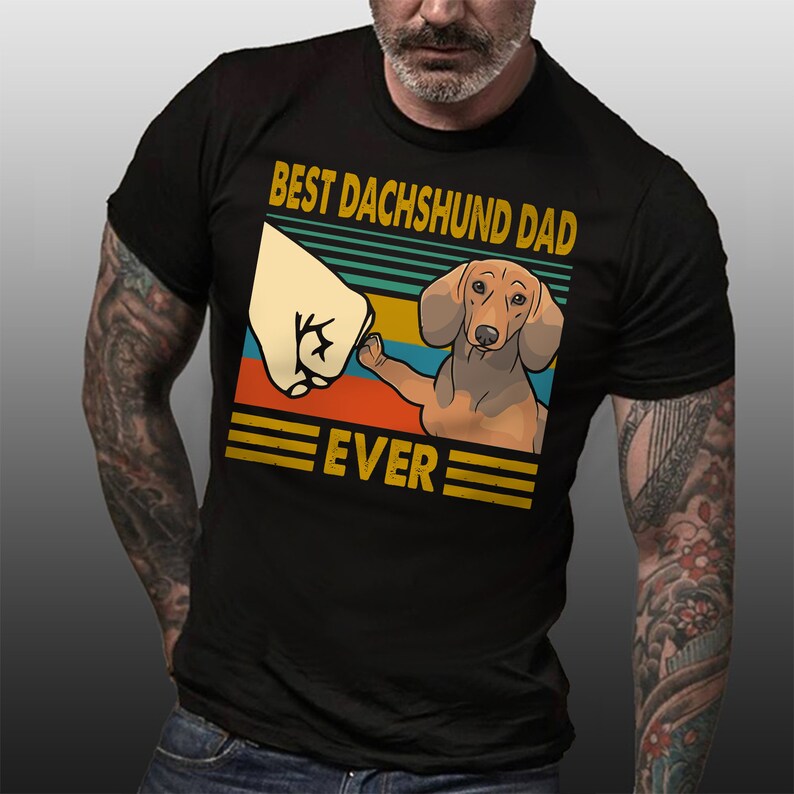 May include: A black t-shirt with a vintage-style graphic of a dachshund giving a fist bump. The graphic says "Best Dachshund Dad Ever".