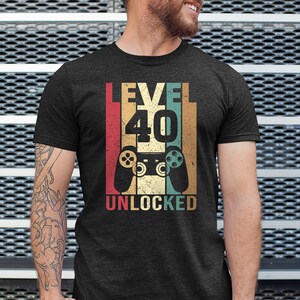 May include: A black t-shirt with a vintage-style graphic that says "Level 40 Unlocked" with a retro video game controller in the center.