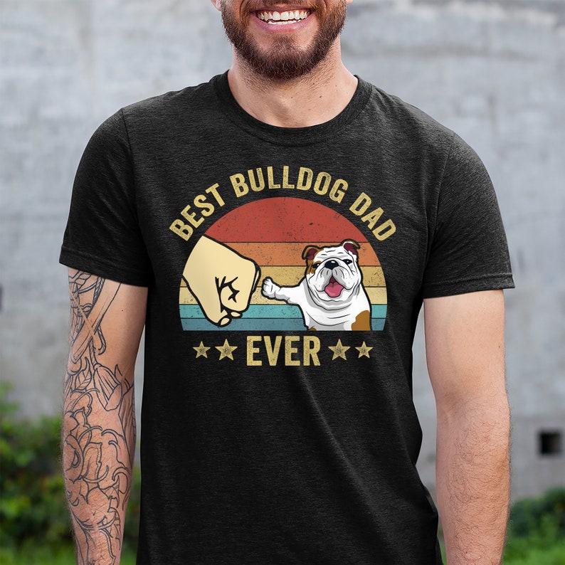 May include: A black t-shirt with a vintage-style graphic that says "Best Bulldog Dad Ever". The graphic features a bulldog with a fist bump and a sunset background.