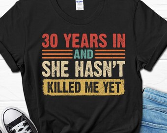 May include: Black t-shirt with a vintage-style graphic that reads "30 Years In And She Hasn't Killed Me Yet".
