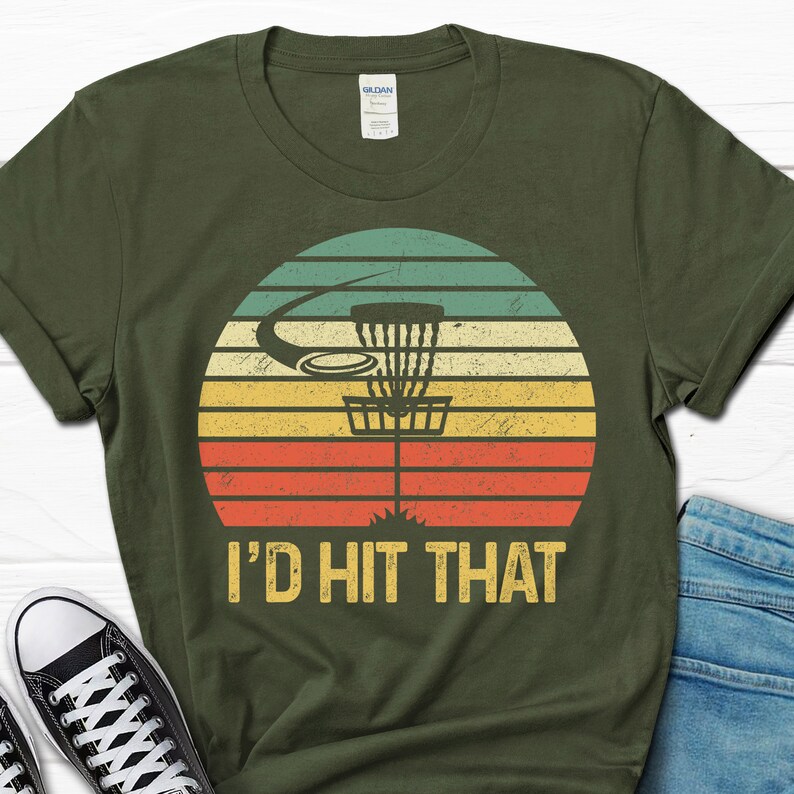 May include: A green t-shirt with a vintage-style graphic of a disc golf basket and the text "I'd Hit That".