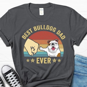 May include: A dark gray t-shirt with a vintage-style graphic that says "Best Bulldog Dad Ever" with a cartoon bulldog and a fist bump.