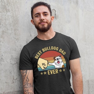 May include: A black t-shirt with a vintage-style graphic that says "Best Bulldog Dad Ever". The graphic features a bulldog giving a fist bump to a hand.