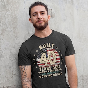 May include: A dark grey t-shirt with a vintage American flag design and the text "Built 40 Years Ago Original & Unrestored - most parts still in working order".