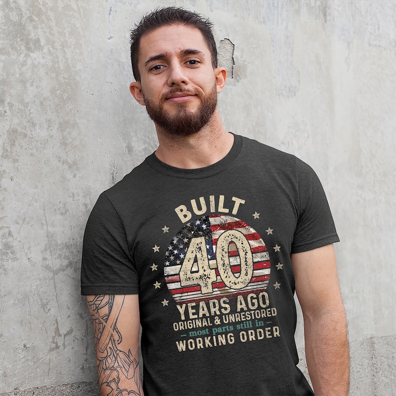 May include: A dark grey t-shirt with a vintage American flag design and the text "Built 40 Years Ago Original & Unrestored - most parts still in working order".