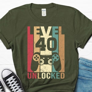 May include: A green t-shirt with a retro-style graphic design featuring a video game controller and the text "Level 40 Unlocked".