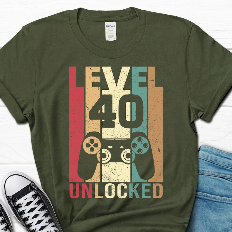 May include: A green t-shirt with a retro-style graphic design featuring a video game controller and the text "Level 40 Unlocked".