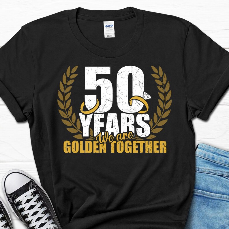 May include: Black t-shirt with a gold graphic that says "50 Years We are Golden Together". The graphic features two gold rings with diamonds and a laurel wreath.