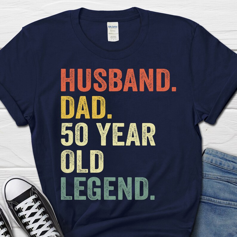 May include: Navy blue t-shirt with a vintage-style graphic that reads "Husband. Dad. 50 Year Old Legend."