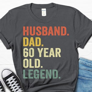 May include: A dark gray t-shirt with a vintage-style graphic that reads "Husband. Dad. 60 Year Old. Legend."