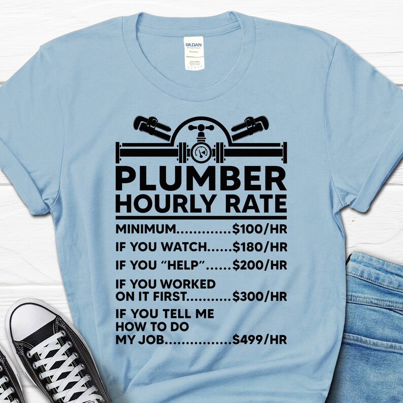 May include: Light blue t-shirt with a black graphic of a plumber's tools and the text "Plumber Hourly Rate". The graphic includes a wrench, pipe, and valve. The text below the graphic lists different hourly rates for a plumber based on the level of assistance provided.  The rates are: Minimum $100/hr, If you watch $180/hr, If you "help" $200/hr, If you worked on it first $300/hr, If you tell me how to do my job $499/hr.