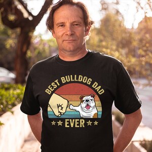 May include: Black t-shirt with a vintage-style graphic of a bulldog giving a fist bump. The graphic says "Best Bulldog Dad Ever" with stars on either side of the word "Ever".