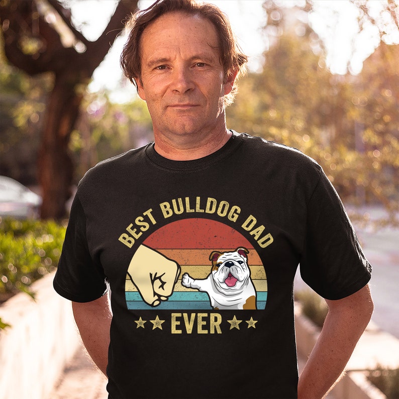 May include: Black t-shirt with a vintage-style graphic of a bulldog giving a fist bump. The graphic says "Best Bulldog Dad Ever" with stars on either side of the word "Ever".