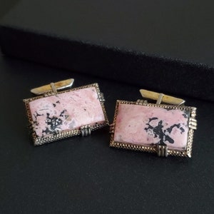 May include: A pair of silver cufflinks with pink and black stone insets. The stones have a marbled pattern.