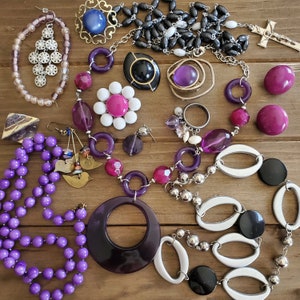 Op de afbeelding: Een verzameling paarse, zilveren en zwarte sieraden met kralen, bedels en hangers. De sieraden zijn gerangschikt op een houten oppervlak.