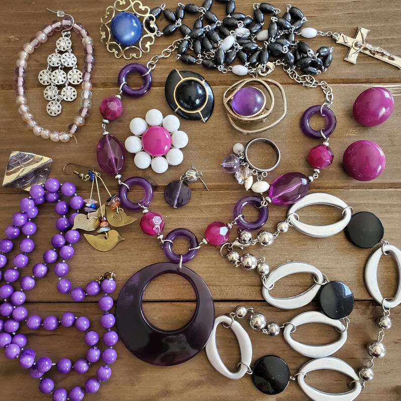 Op de afbeelding: Een verzameling paarse, zilveren en zwarte sieraden met kralen, bedels en hangers. De sieraden zijn gerangschikt op een houten oppervlak.