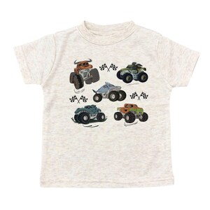 Puede incluir: Camiseta beige claro con un gr&aacute;fico colorido de seis monster trucks. Cada cami&oacute;n tiene un dise&ntilde;o &uacute;nico, incluyendo un tibur&oacute;n y patrones de camuflaje. Banderas a cuadros blancas y negras est&aacute;n dispersas alrededor de los camiones.