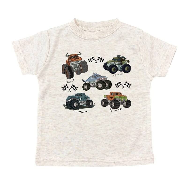 Puede incluir: Camiseta beige claro con un gr&aacute;fico colorido de seis monster trucks. Cada cami&oacute;n tiene un dise&ntilde;o &uacute;nico, incluyendo un tibur&oacute;n y patrones de camuflaje. Banderas a cuadros blancas y negras est&aacute;n dispersas alrededor de los camiones.