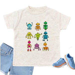 May include: A light gray t-shirt featuring a colorful robot design. The shirt is paired with denim shorts and light blue sneakers with orange soles. The robots are in various colors and designs.