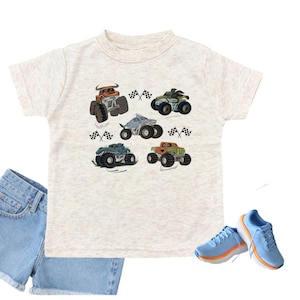 Puede incluir: Camiseta beige claro con un estampado de seis monster trucks y banderas a cuadros. El conjunto incluye pantalones cortos de mezclilla y zapatillas de deporte azul claro con suelas naranjas, creando un conjunto l&uacute;dico.