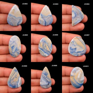 May include: Nine polished gemstones in various shapes, including teardrop and oval. The stones feature a swirling pattern of blue, cream, and white, with a polished, glossy finish. Each stone is held in a hand against a black background.