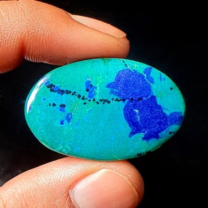 May include: Oval shaped cabochon gemstone with a blue and green pattern. The stone has a dark blue center with a green outer edge. The stone is set in a silver ring.