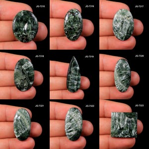 May include: Collection of nine polished seraphinite gemstones in various shapes, including oval, teardrop, and rectangular. The stones display a dark green color with silvery, feathery inclusions. Each stone is held in a hand against a black background.